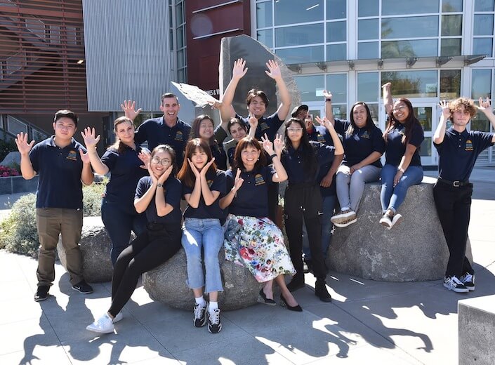 A group of Welcome Center Ambassadors and Julie Vu pose in a group wearing blue polo shirts.