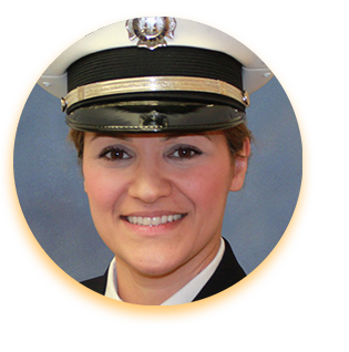 Soulmaz Brazil, a young woman posing in a fire service uniform and smiling. Her dark hair is pulled up under her military-style hat, and her skin is tan.