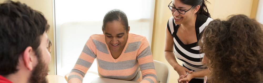 Four students work together a desk in a classroom over a laptop.