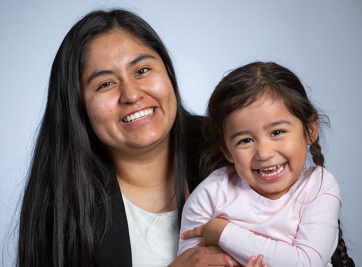 Latina mom and toddler girl pose and smile.