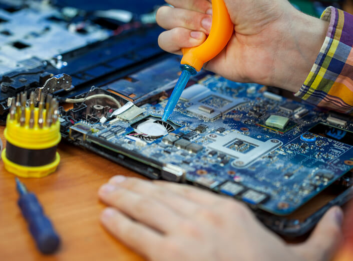 A pair of male hands with light skin work on a circuit board.