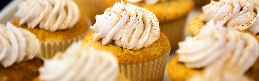 A tray of cupcakes is pictured, they have white frosting with cinamon sprinkled over them.