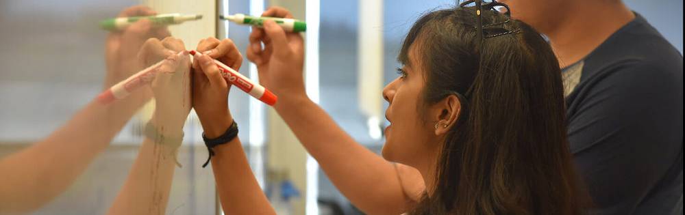 A young man and a young woman work at a classroom marker board.