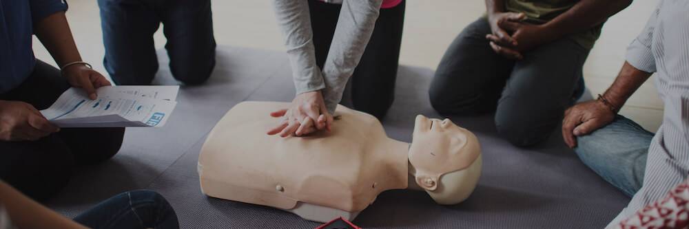 Students demonstrate CPR moves on a dummy in a semi-circle.