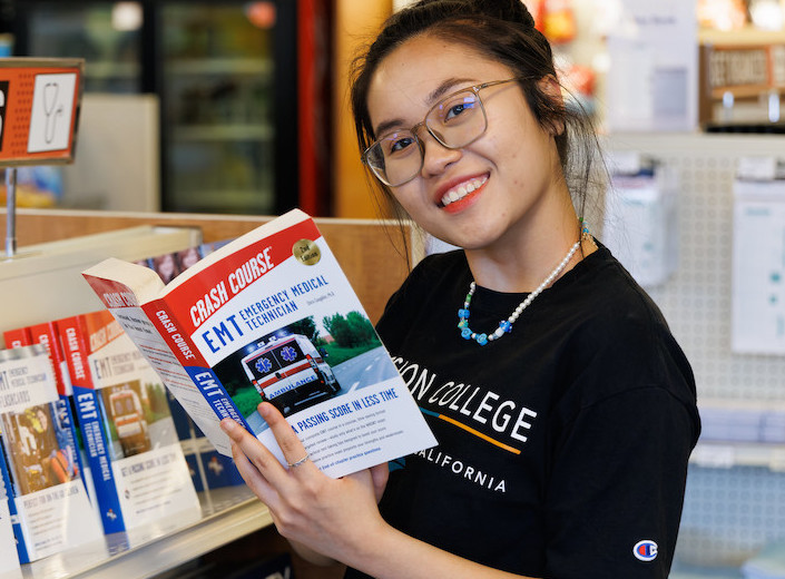 Young woman of Asian descent holds a text for EMTs.