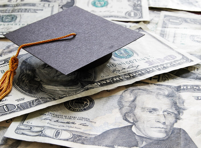 A commencement cap sits on top of a pile of cash.