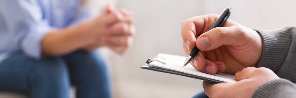 Specialist noting problems of young woman at psychotherapy session.