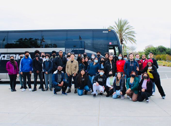 A group of students (male, female, students of color) are posed in a group outside on campus in casual clothes on their way to a college tour of UC Berkeley..