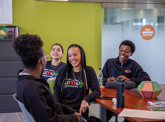 Umoja classroom. Students sit at table in classroom and wear Umoja polo shirts.