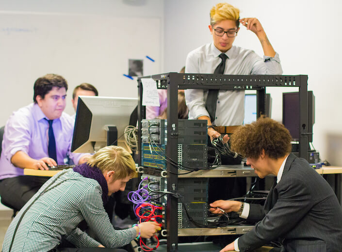 Group of young men and women work on a server in a classroom.