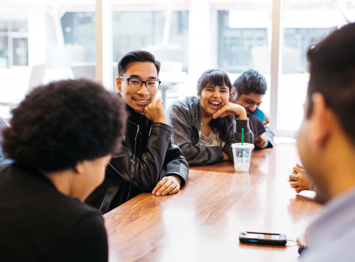 Year Up Program. Young adults work together in a casual business environment at a big table in a modern office building.