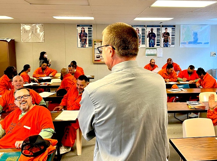 Professor instructs class of men in orange jumpsuits.